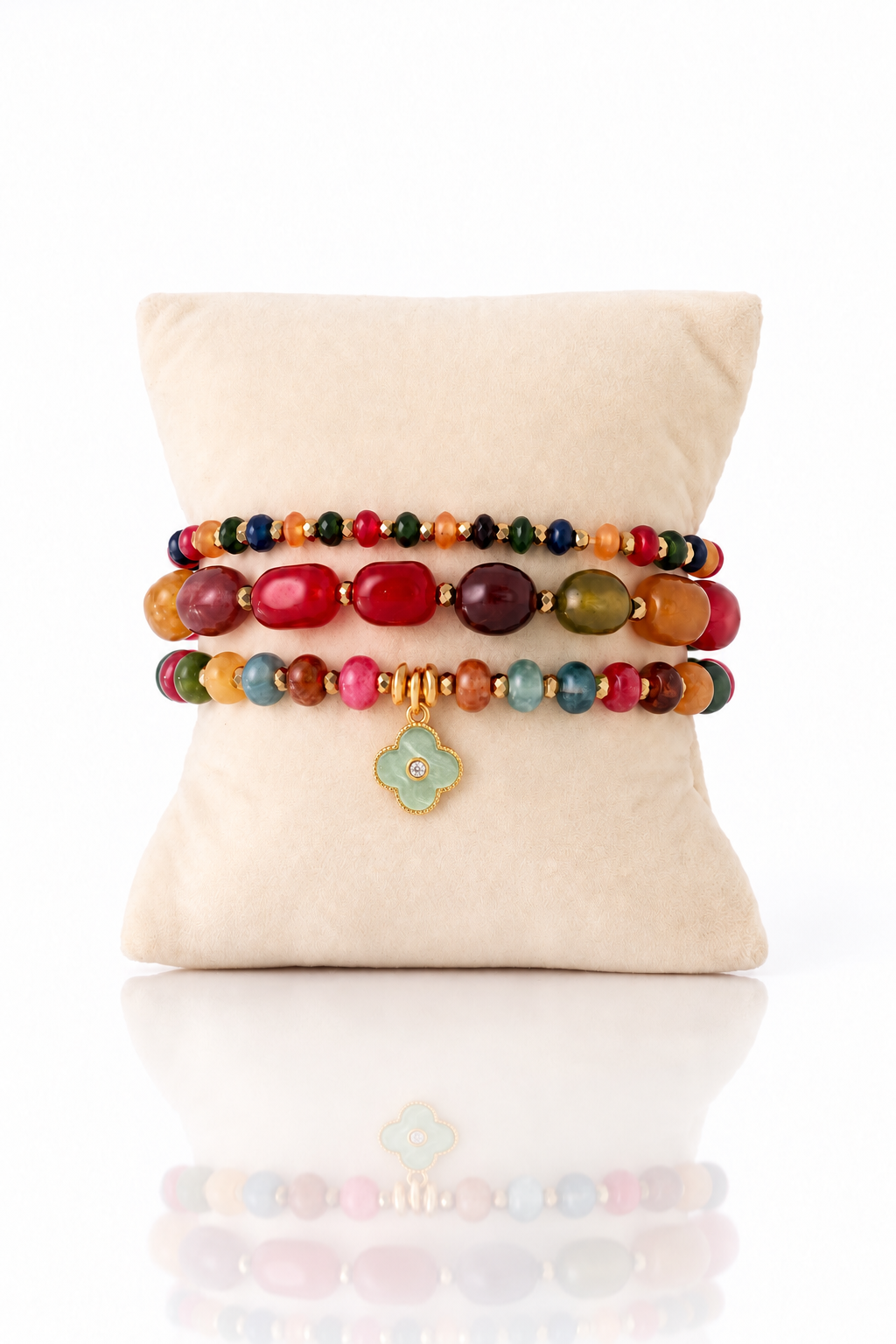 Autumn Jewels three-bracelet set with multicolored beads and a seafoam clover charm on a cream cushion