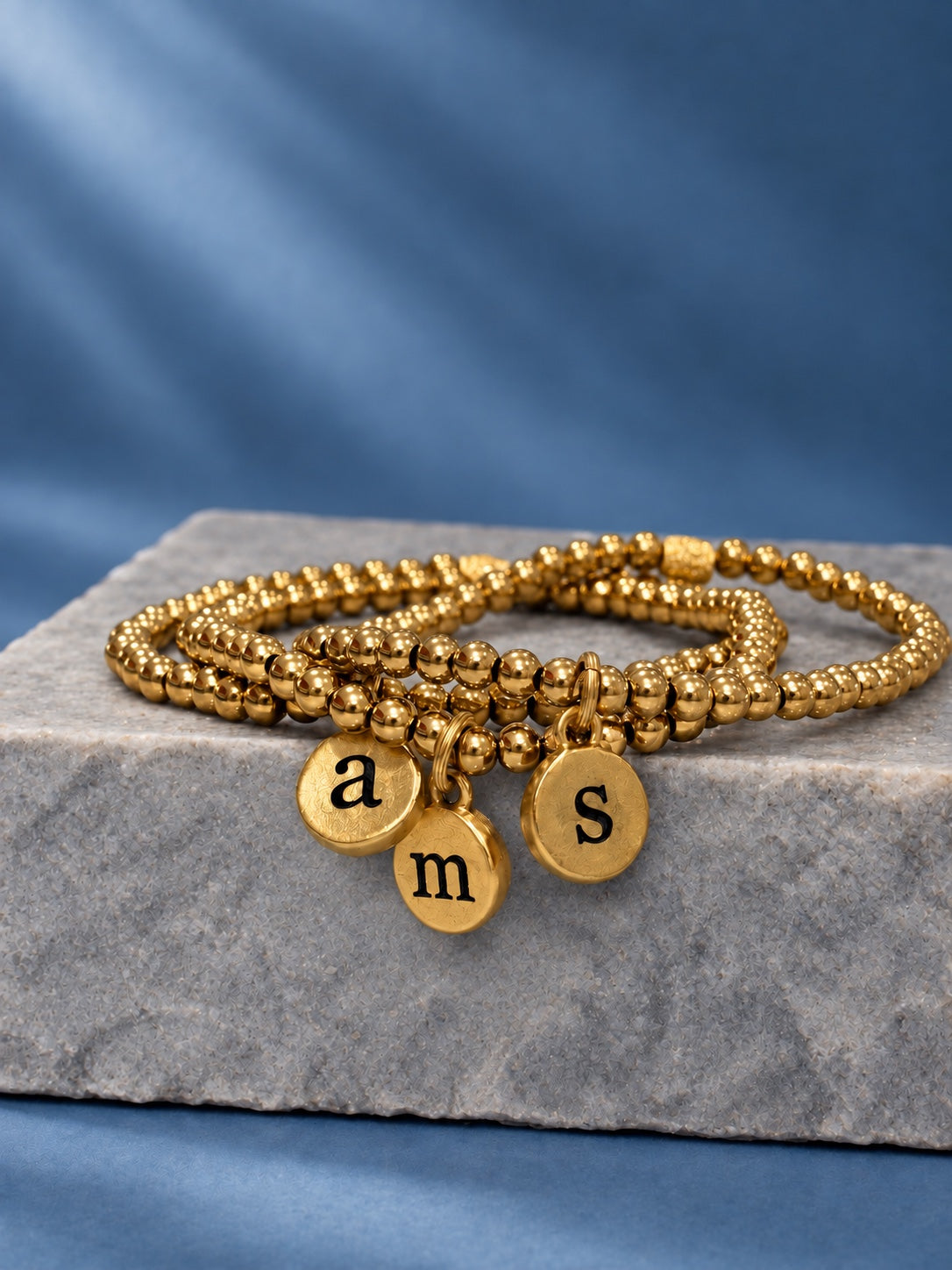 gold initial pendant bracelets on blue background